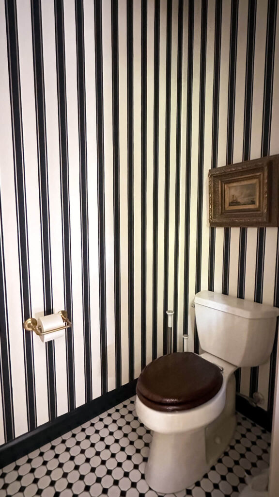 Primary bathroom renovation reveal. A toilet room with black and white checkered tile flooring and striped wallpaper.